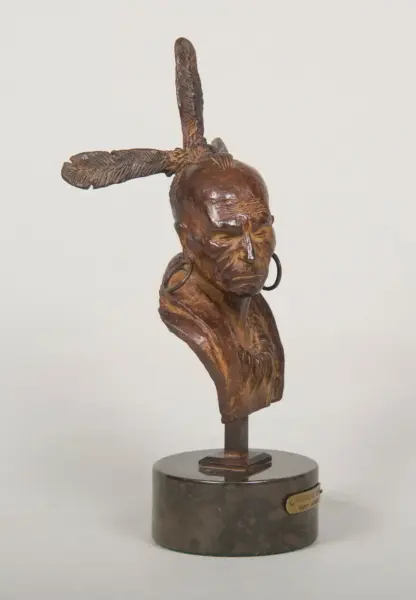 Bronze bust of a Native American man with a tall feather headdress and hoop earrings on a round pedestal.