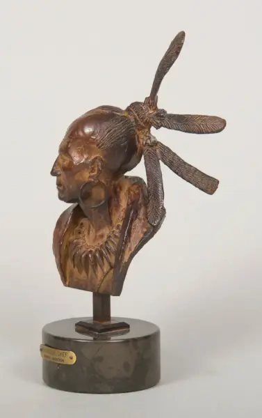 Bronze sculpture bust of a Native American man with a tall feathered headdress, mounted on a cylindrical base with a brass plaque.