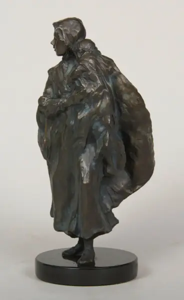 Bronze sculpture of a cloaked figure standing on a round base, facing left with a hooded head and folded arms.