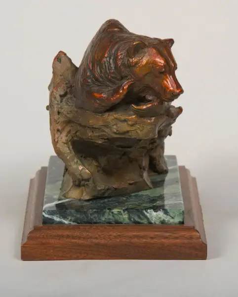 Bronze bear head sculpture on a rocky base set on a green marble pedestal with a wooden plinth.