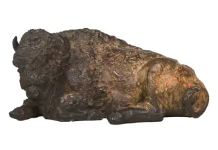 Bronze sculpture of a reclining buffalo with a textured, rough surface and curled horns.