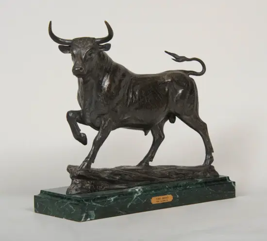 Bronze bull sculpture with a raised front leg on a rocky base, mounted on a green marble pedestal with a plaque.