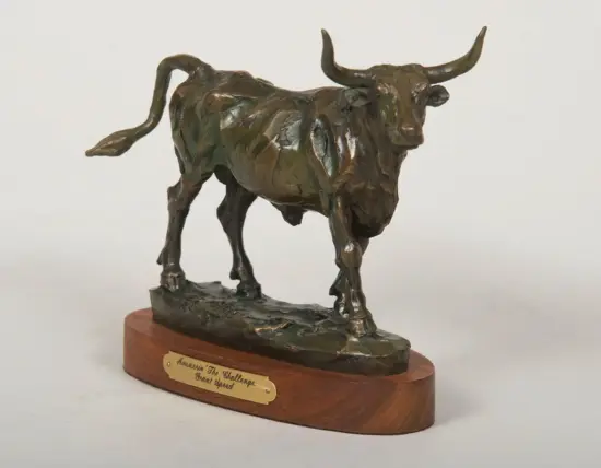 Bronze sculpture of a bull standing on a wooden base, with a plaque at the front (art statue on display).