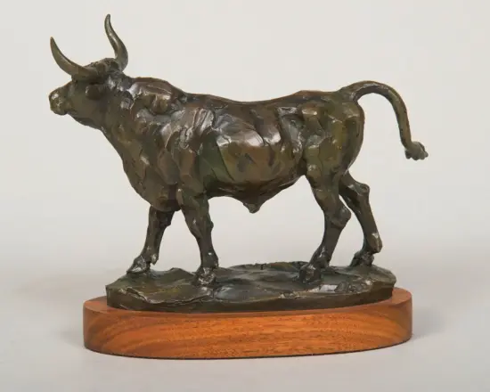 Bronze sculpture of a bull with a textured surface, standing on a wooden pedestal.