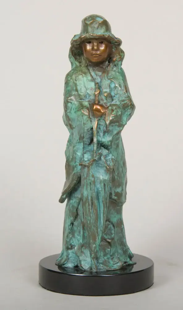 Bronze sculpture of a hooded figure in a cloak, holding a staff, with a green patina on a black circular base.