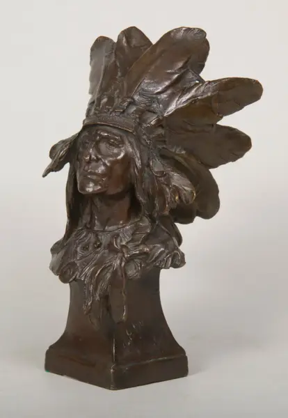 Bronze bust of a Native American man wearing a feathered headdress, mounted on a square pedestal.