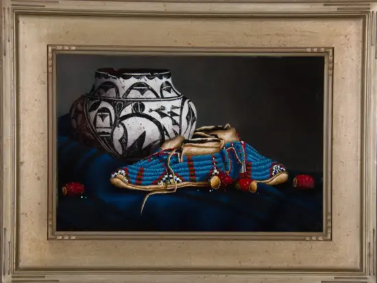 Framed still life: a large black‑and‑white patterned vase sits beside blue beaded moccasins on a dark blue cloth.