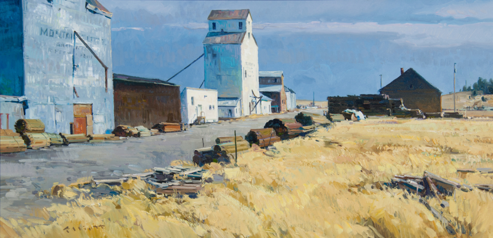 Rural industrial yard with a tall white silo and blue/white warehouses along a dusty road, with stacked lumber nearby and a clear blue sky above.