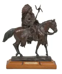 Bronze statue of a Native American warrior on horseback with a feathered headdress, holding a staff, mounted on a wooden base with a plaque reading 'American Warrior'.