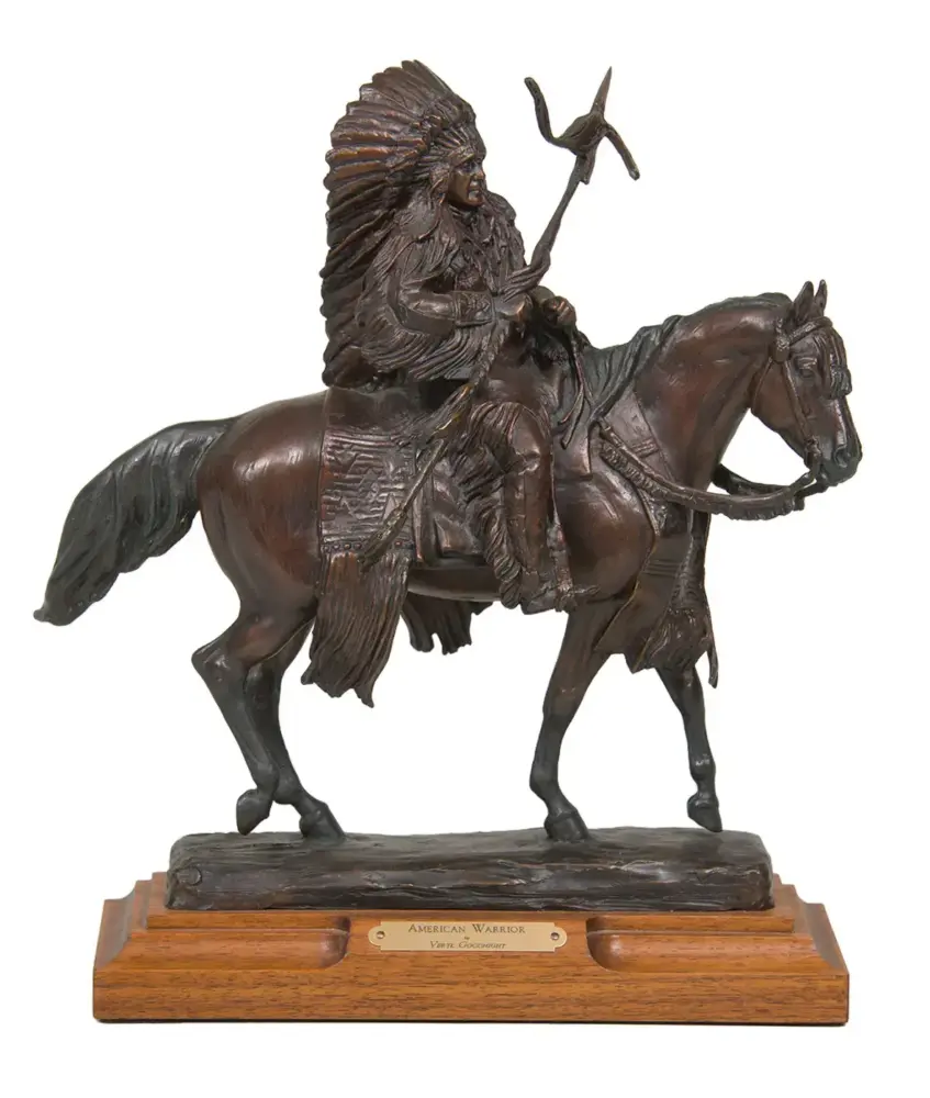 Bronze statue of a Native American warrior on horseback with a feathered headdress, holding a staff, mounted on a wooden base with a plaque reading 'American Warrior'.