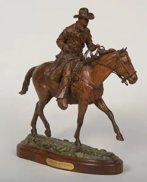 Bronze statue of a cowboy on a rearing horse, holding a lasso, mounted on a wooden base with a plaque.