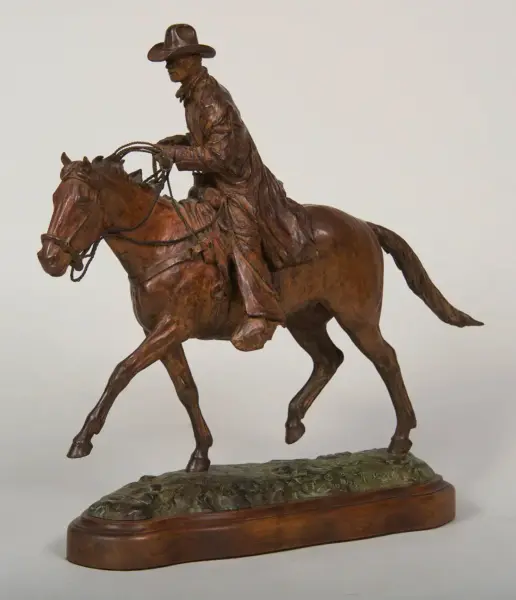 Bronze sculpture of a cowboy riding a rearing horse on a wooden base with rope in hand