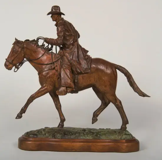 Bronze statue of a cowboy riding a rearing horse, mounted on a wooden base with a textured ground.