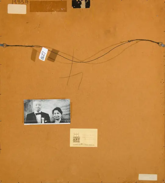 Back of a wooden mounting board with two facing wires across, a small black-and-white photo of a man in a tuxedo and a woman, and several labels/cards attached.