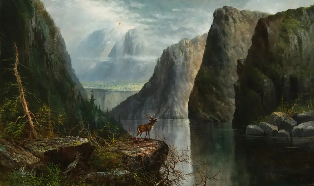 A deer stands at the edge of a calm river amid towering rocky cliffs and misty mountains in a dramatic canyon landscape.