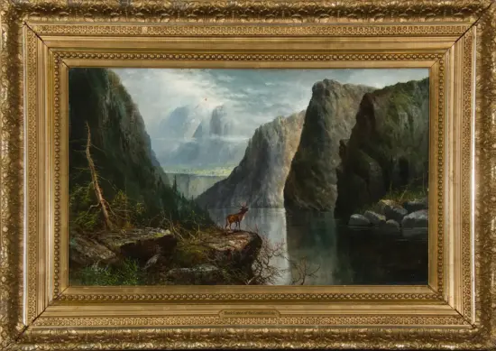 A landscape painting of a deer standing on a rocky shore, with towering cliffs, a calm lake, and misty mountains in the distance inside an ornate gold frame.