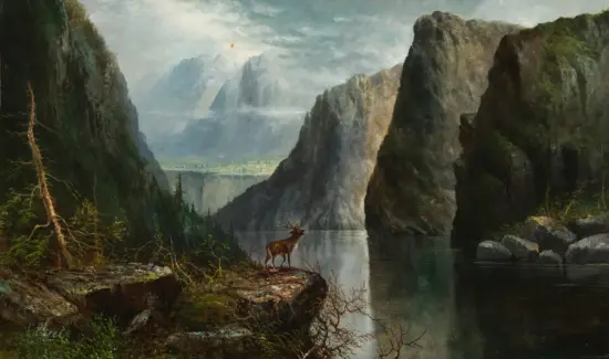 A deer stands at the edge of a calm river amid towering rocky cliffs and misty mountains in a dramatic canyon landscape.