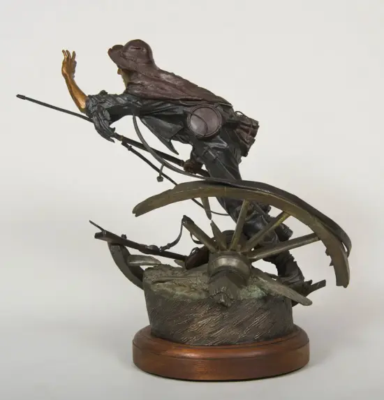 Bronze statue of an adventurer wearing a hat and cloak, riding a spoked wheel contraption on a rocky base.