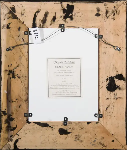 Back of a framed painting showing hanging wire, metal brackets, and a label with 'Krystii Melane Black Fancy' on white paper panel.