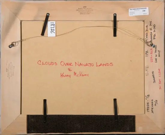Back of a framed artwork titled 'Clouds Over Navajo Lands' by Kenny McKenna, with hanging wire and handwritten notes visible on the edges.
