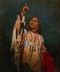 Native American man in colorful ceremonial regalia raises one finger toward the sky, looking up.