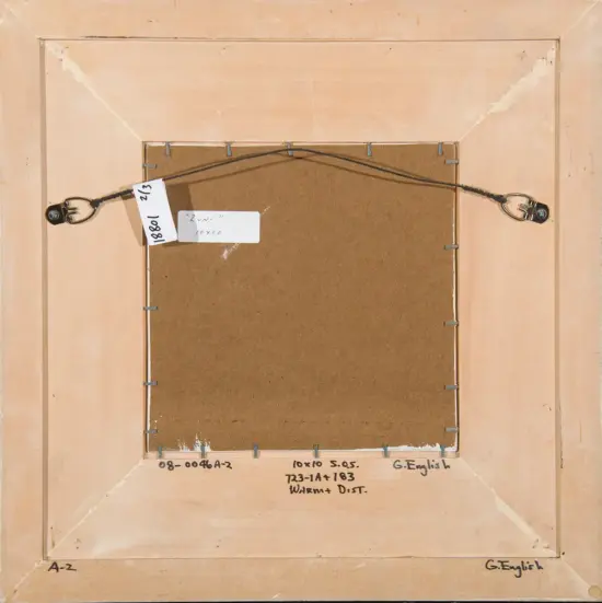 Back of a framed artwork showing a wire hanging system and labels on the frame’s edges, with a brown backing board and handwritten notes along the bottom edge.