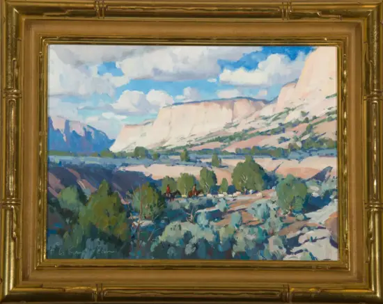 Painting of a canyon landscape with layered cliffs, blue sky and white clouds, and two riders on a dirt path in the foreground, in a gold frame.