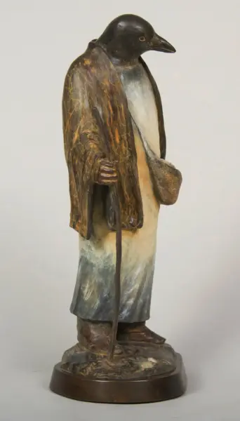 Wooden sculpture of a man with a duck head, wearing a long weathered coat and holding a cane, on a round base.