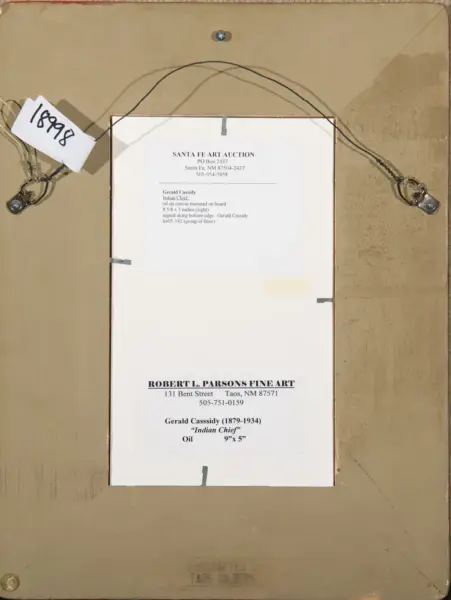Back view of a framed artwork with a typed auction label from Santa Fe Art Auction and another label for Gerald Cassidy, Indian Chief, oil, 9"x5" (back of frame).