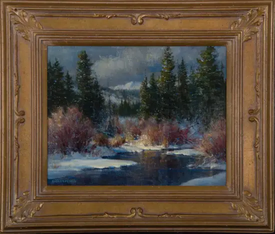 Winter landscape painting of evergreen trees beside a partially frozen stream, snow on the ground, under a cloudy sky, in a gilded frame.