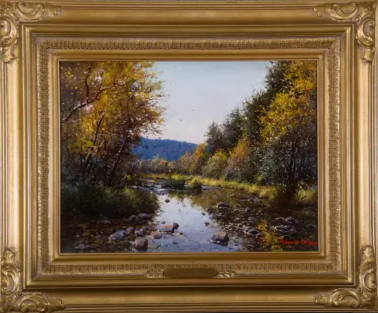 Autumn landscape painting of a rocky creek with gold and orange trees, and distant blue hills, in a gilded frame.