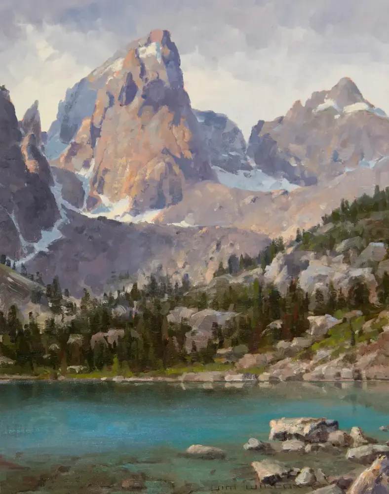 Mountain landscape with jagged peaks, evergreen forest, and turquoise lake in a rocky valley.