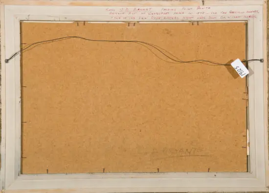Back of a framed artwork: brown backing board with a hanging wire across the top, mounted in a light wood frame; a small white tag with numbers hangs on the right end. Handwritten red text is visible along the top edge.