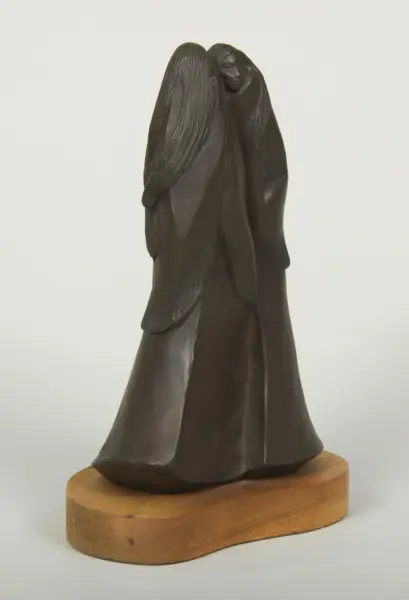 Dark metal sculpture of an angel with large wings standing on a wooden base.