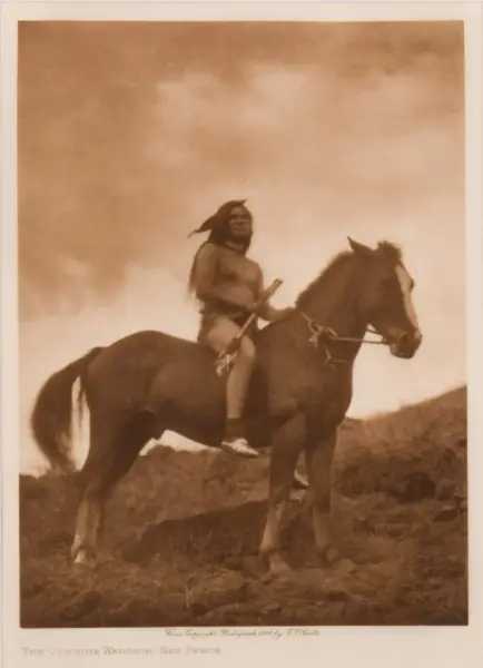 Sepia-toned photograph of an old-time Native American warrior bare-chested, riding a horse across a grassy hillside, holding a spear.