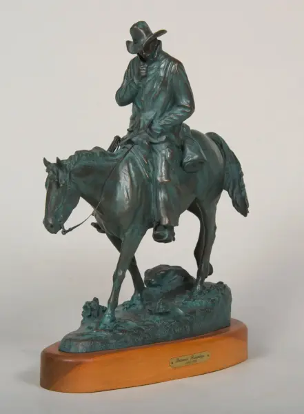 Bronze statue of a cowboy in a wide-brim hat riding a horse, mounted on a wooden base.