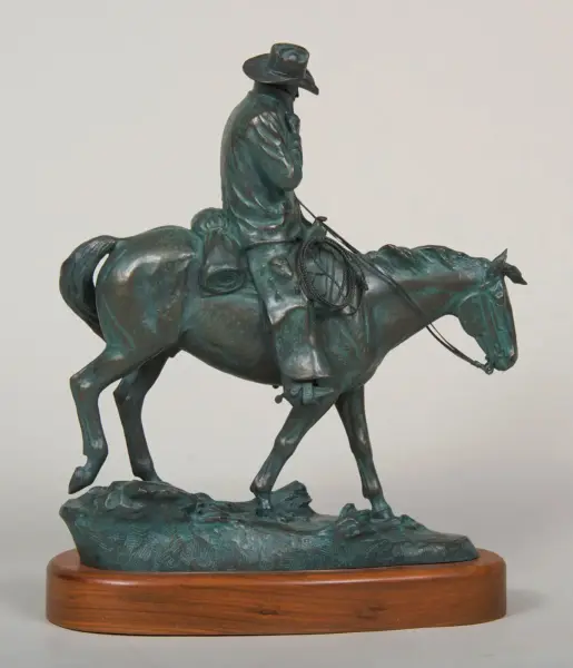 Bronze sculpture of a cowboy on a horse, holding a rope, mounted on a wooden base.