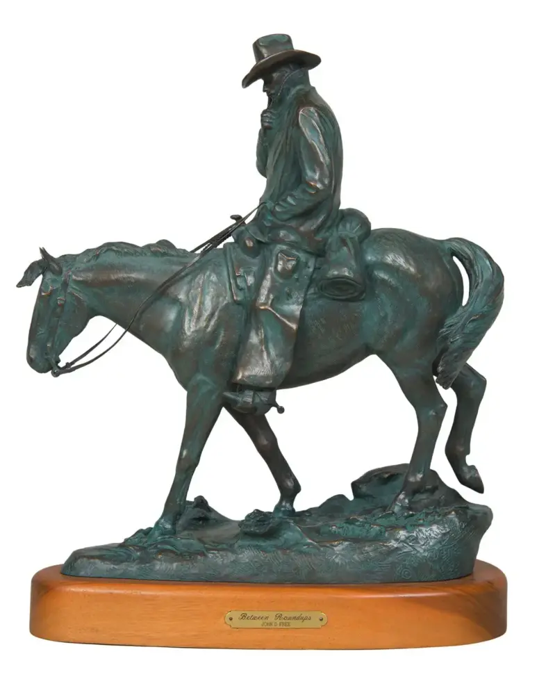 Bronze statue of a cowboy on a horse, mounted on a wooden base.