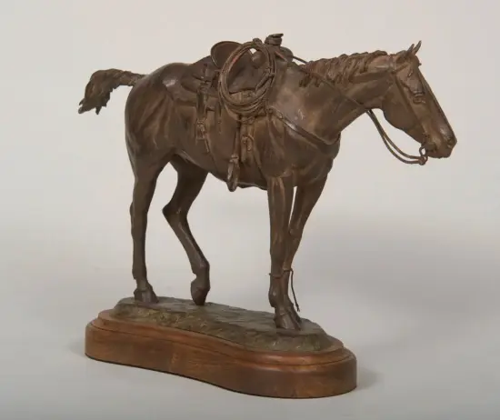 Bronze statue of a saddled horse with rope draped over its back on a wooden pedestal