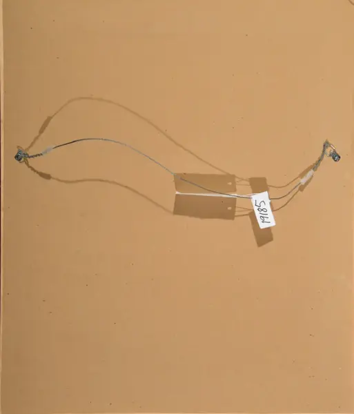 Two small electrical wires with metal connectors at each end, taped in the middle on a brown surface with a handwritten tag reading 19/85.
