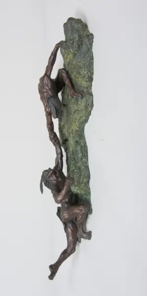 Bronze sculpture of two intertwined climbers gripping a jagged green rock
