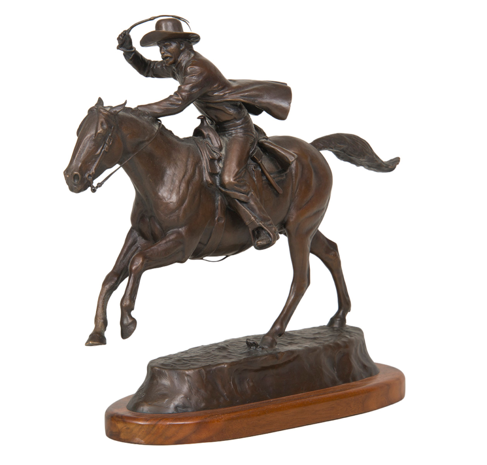 Bronze statue of a cowboy riding a rearing horse, lasso raised, on a rocky pedestal.
