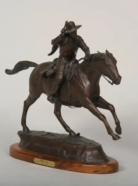 Bronze equestrian statue of a cowboy on a rearing horse, mounted on a wooden base with a plaque.