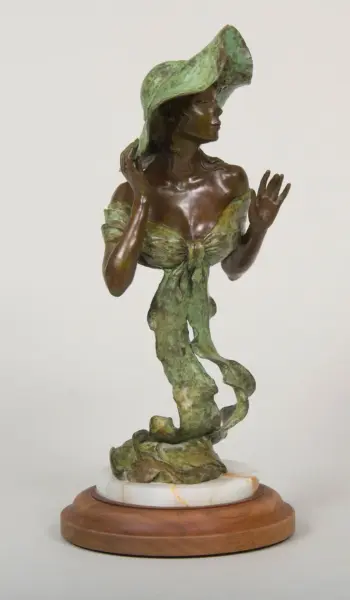 Bronze statue of a woman in a wide green hat and flowing green dress, displayed on a wooden pedestal with a marble base.
