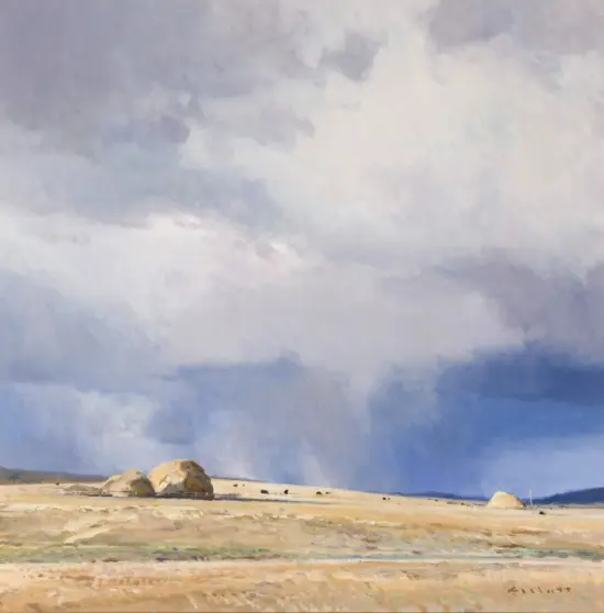 Coastal scene with a sandy shore, large rocks near the water, and a cloudy blue sky.