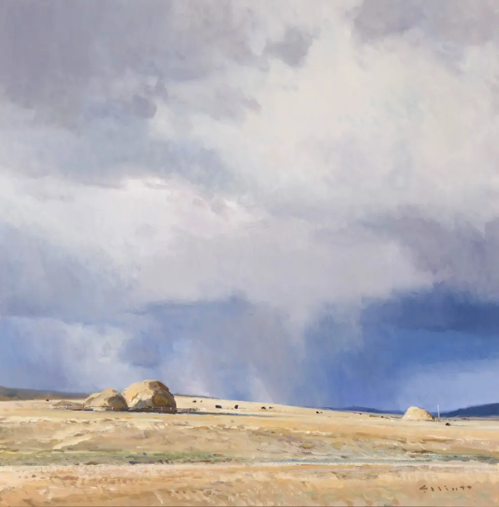 Coastal scene with a sandy shore, large rocks near the water, and a cloudy blue sky.