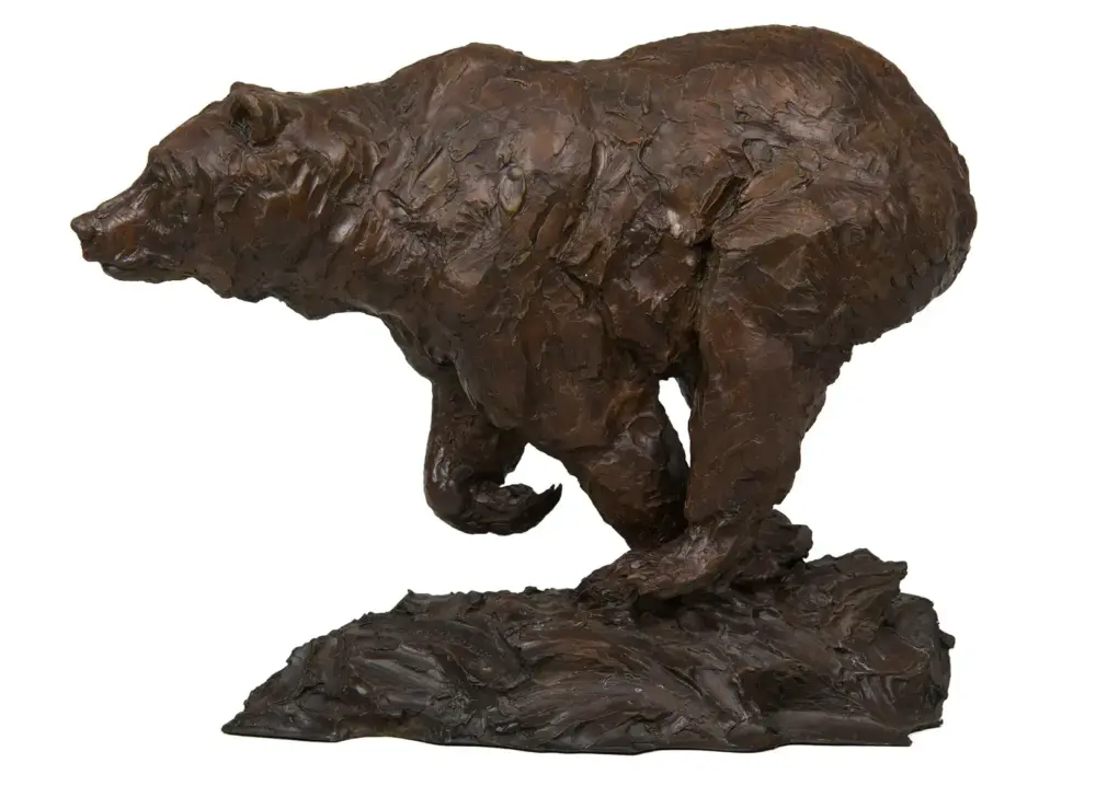 Bronze-style bear sculpture with rough texture standing on a rocky base, viewed from the side
