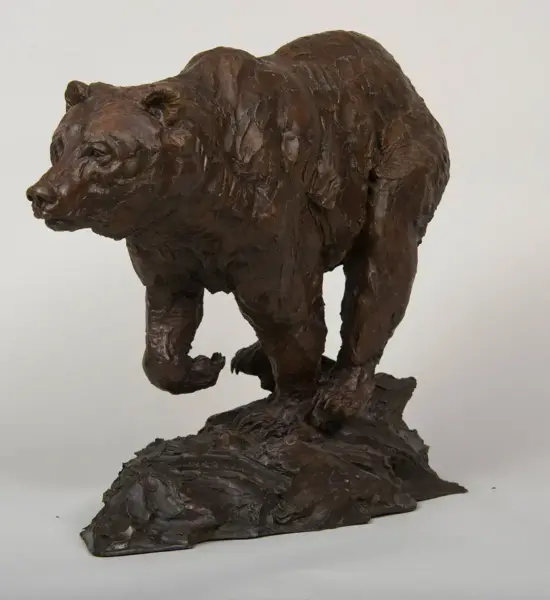 Dark brown sculpture of a bear standing on a rocky base, appears to be in motion as if stepping forward