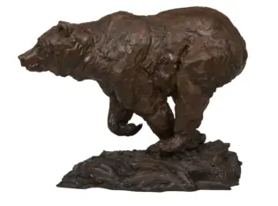 Bronze-style bear sculpture with rough texture standing on a rocky base, viewed from the side