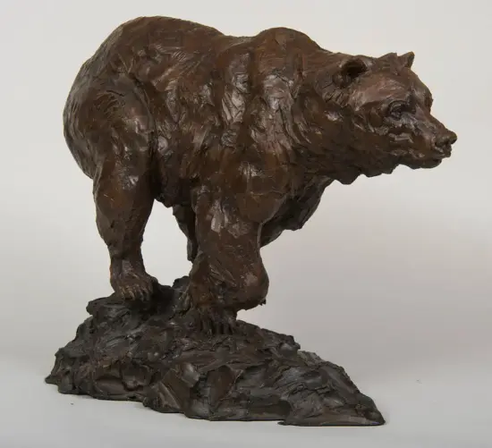 Brown bear sculpture standing on a jagged rocky base, with a textured, rugged surface.